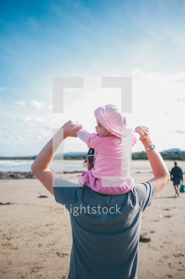 infant girl on her father's shoulders at the beach 