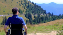 Optimistic handicapped man sitting on wheelchair admiring nature on the mountain. Travel and freedom concept. Hand held shot