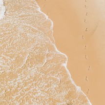 A path of footprints in the sand on a beach by the waves of the Pacific Ocean	

