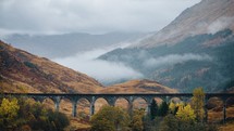 A view of the Glenfinnan viaduct train bridge in Scotland with foggy mountains behind it