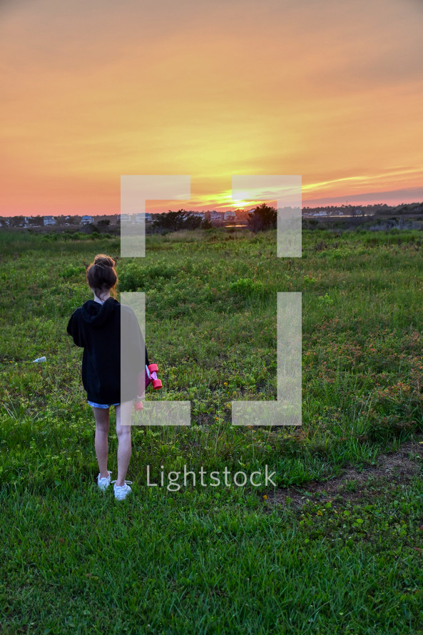 girl standing a skateboard looking out at the sunset over the intracoastal waterway with copy space 