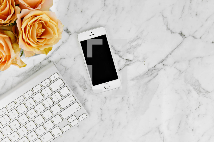 cellphone, computer keyboard, and yellow roses on a marbled background 