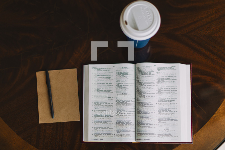 open Bible, notepad, pen, and coffee cup on a table 