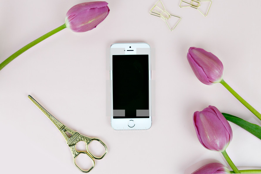 iPhone, scissors, gold paperclips, and fuchsia tulips on a pink background 