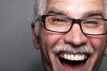 The face of a laughing, middle aged man wearing glasses.