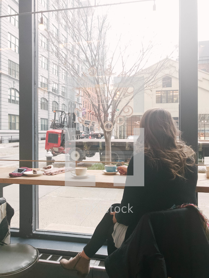 a woman sitting in a window seat of a coffee shop 