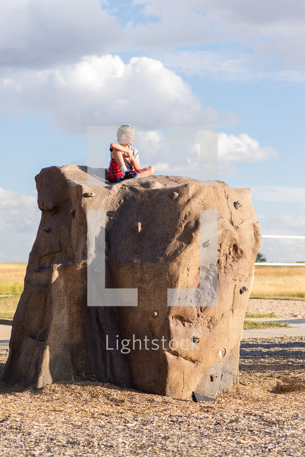 a boy child sitting on a rock outdoors 