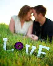 word LOVE in the grass in front of a couple looking into each other's eyes