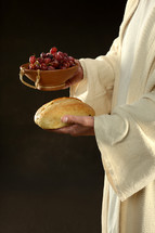 Jesus' hands holding a loaf of bread and a bowl of grapes.