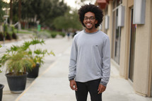 A smiling young man standing on a sidewalk.