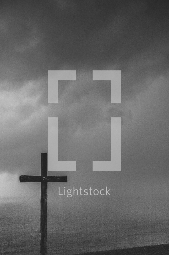 Wooden cross under a stormy sky at the ocean.