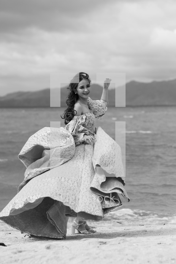 a woman dancing on a beach in an elegant gown 