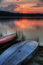 Kayaks on lake shore at sunset.