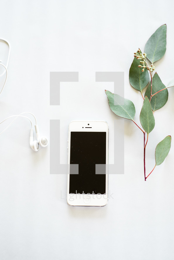 Earphones, a cell phone, and a sprig of green leaves on a white background.