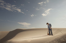 man holding a guitar by the neck standing on sand dunes