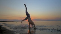 Athlete doing acrobatic tricks on the beach at sunset