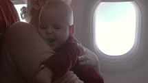Mother with six months old baby daughter traveling by plane. Woman holding quiet child in arms and stroking her back