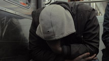 Slow motion shot of unidentified homeless man in shabby clothes dozing during subway ride. He sitting with face hidden under the hood