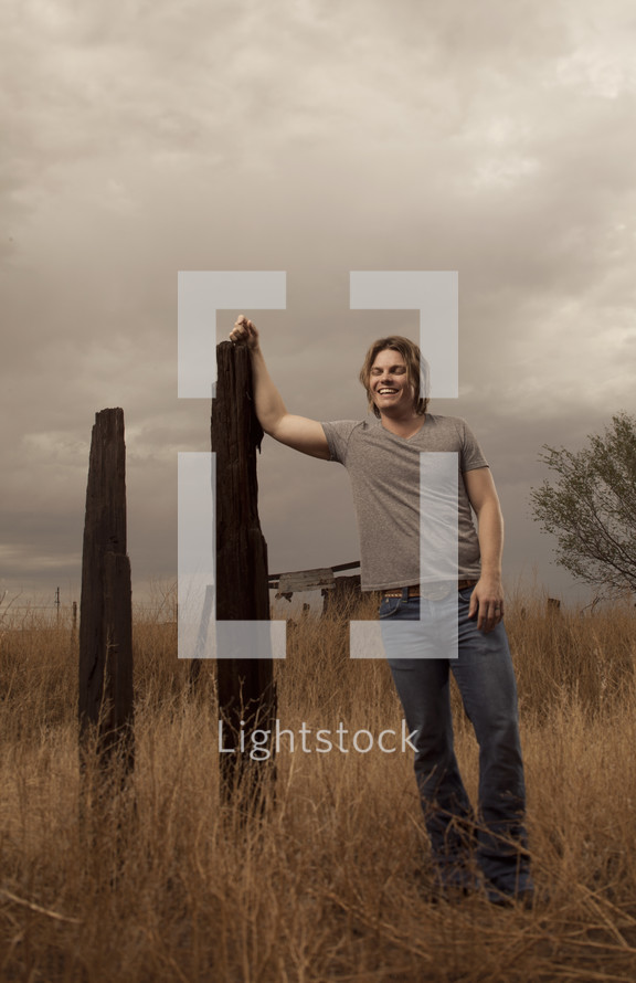 man leaning against an old fence post 
