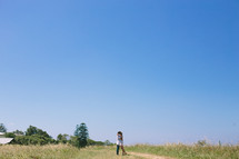 Couple hugging while standing on a dirt road in a grassy field.