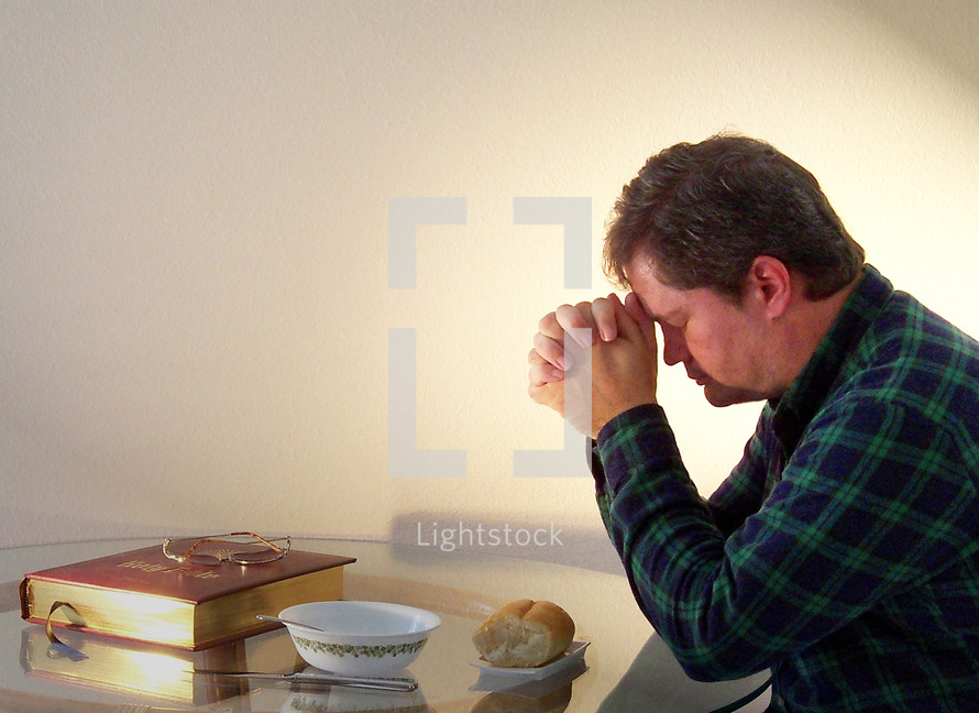 A young man bows and gives thanks in prayer surrounded by a loaf of bread and the word of God, our daily bread for living surrounded by a glowing light.