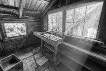 Black and white image of the interior of an abandoned cabin with sunrays