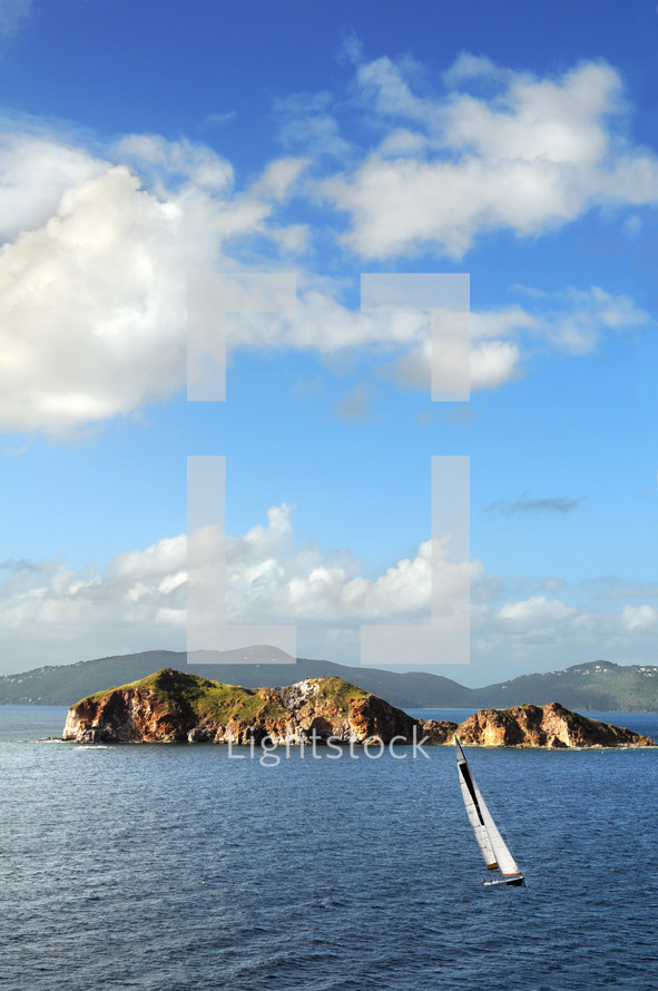 Rock islands in a ocean, with a sailboat in the water, mountains in the background