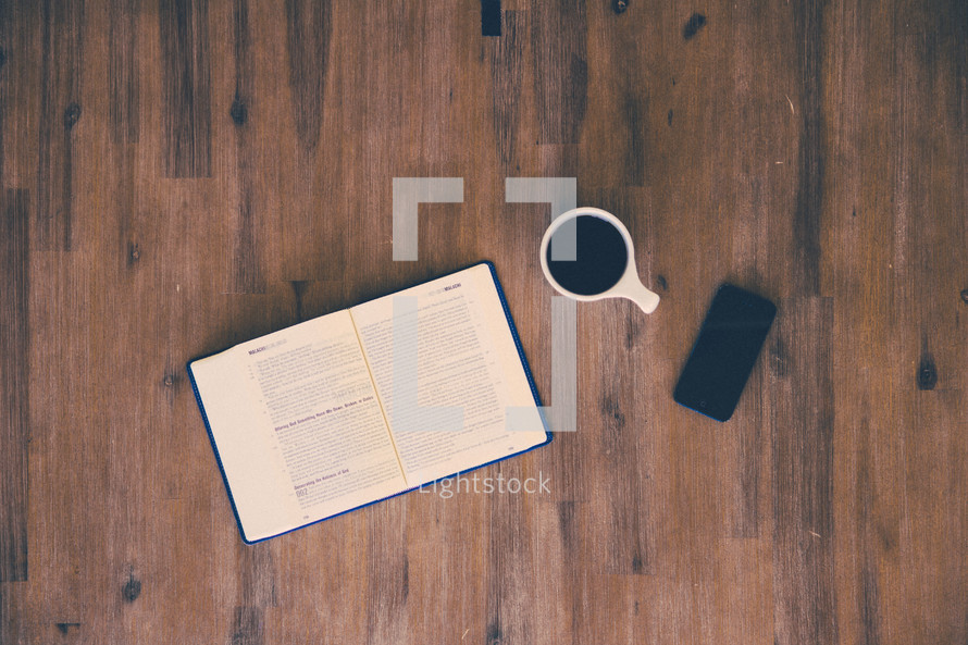 open Bible, cellphone, and coffee mug on a wood table 