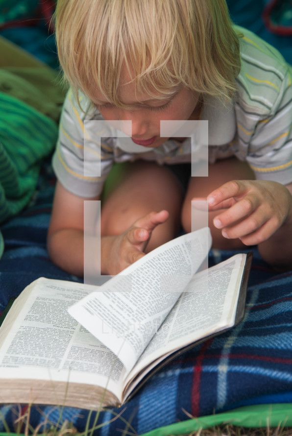 child reading a Bible in a tent and sleeping bag