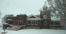 An old, brick church building with slow motion snow flakes falling. Snowflakes fall in dramatic, cinematic slow motion.