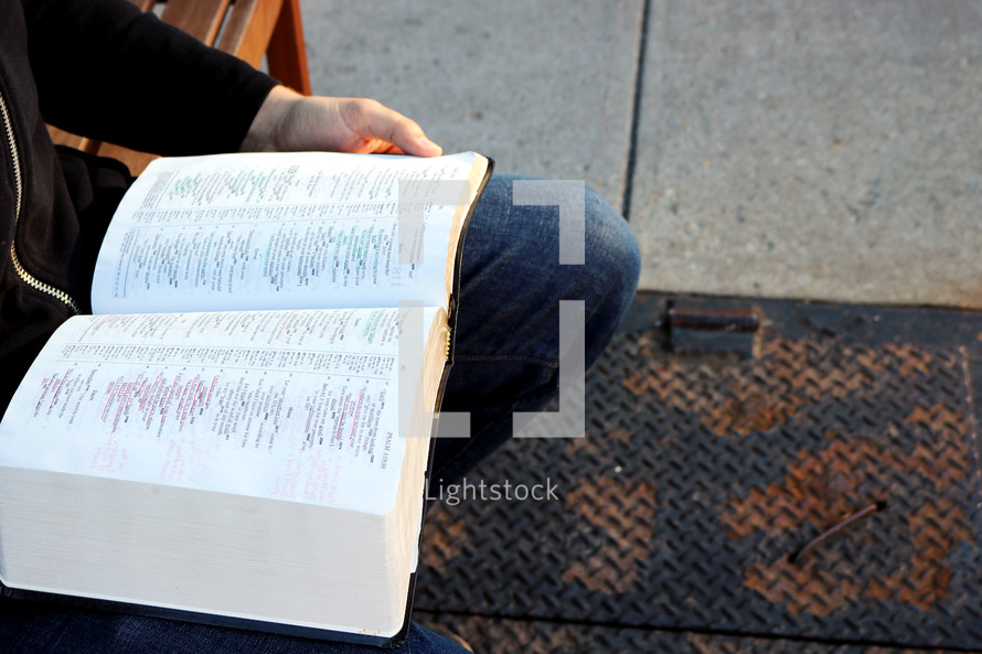 a man reading a Bible with notes while sitting on a bench 