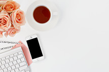 phone, computer keyboard, pencils, tea cup, and peach roses on a desk 