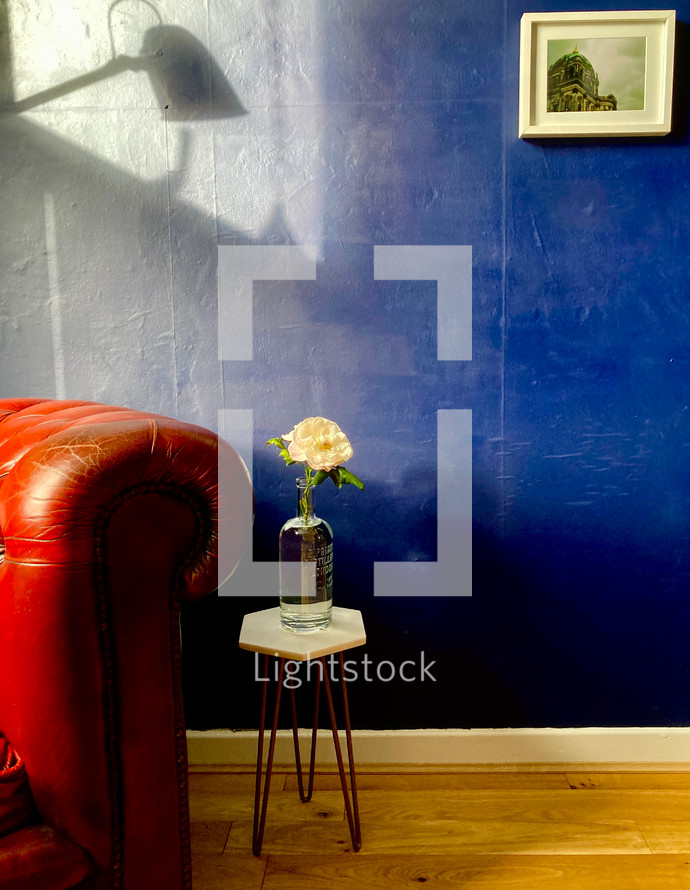 Red couch with white flower in vase and a blue wall background
