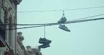 A pair of sneakers hangs from electric wires between two buildings on a rainy day