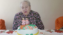 Elderly woman blowing out birthday candles.