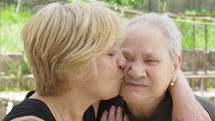 Middle aged woman kisses an elderly woman on the cheek.