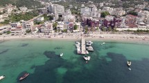Spile Beach Coastline With Boat Pier In Himare Beside Turquoise Waters Of The Ionian Sea. Aerial Pan Left
