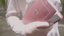 a woman walking in the park carrying a Bible 