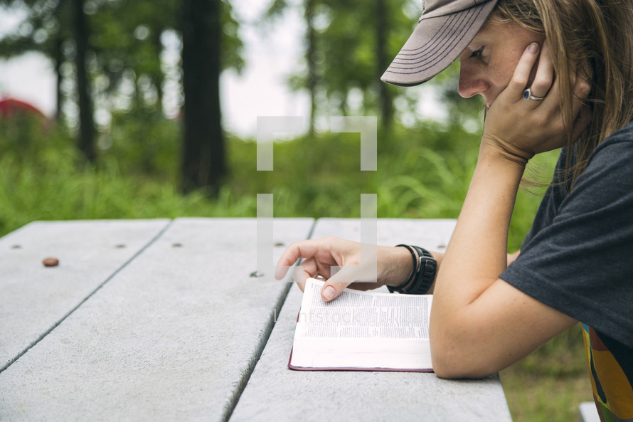 A young woman reading the Bible at a picnic table.