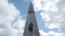 statue in front of a Church steeple in Iceland and clouds passing by 