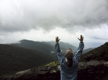 woman standing on a mountain top with raised arms 