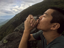 man with praying hands on a mountain top 