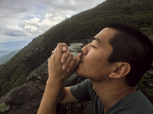 man with praying hands on a mountaintop 