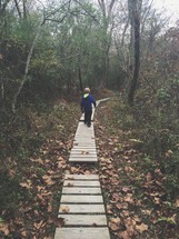 boy child walking on wood boards along a nature trail 