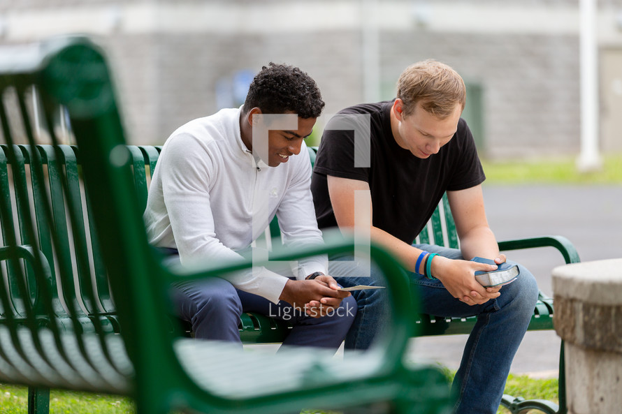 Two men sitting on a park bench praying together