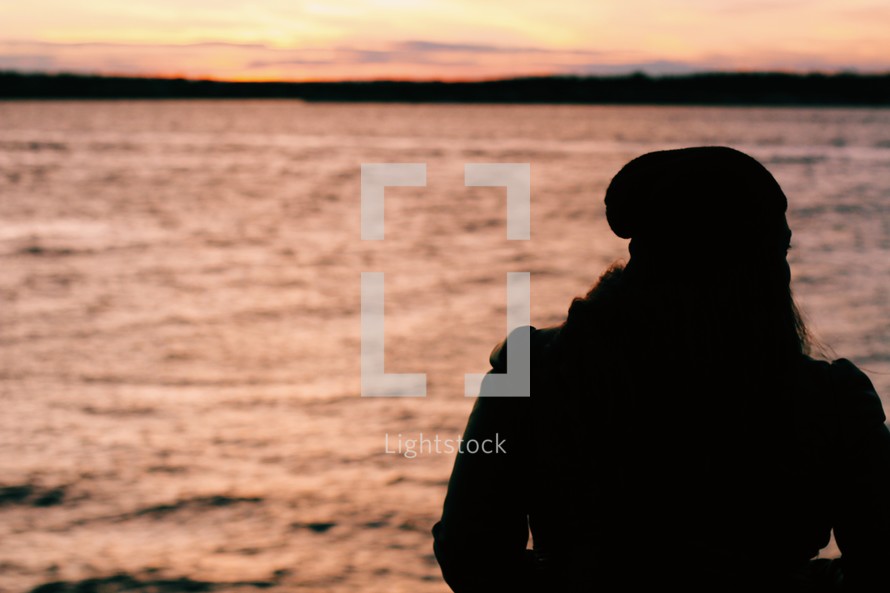 silhouette of a woman looking out at water at sunset 