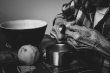 elderly woman sitting at a kitchen table peeling apples 