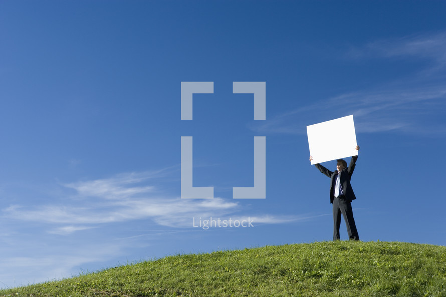 Businessman holding a placard on the top of a hill themes of placard advertisement copy space 
