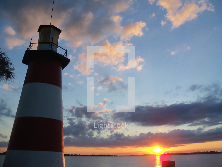 A beautiful red and white lighthouse at sunset overlooking the water against a blue, purple and orange sky at sunset. 