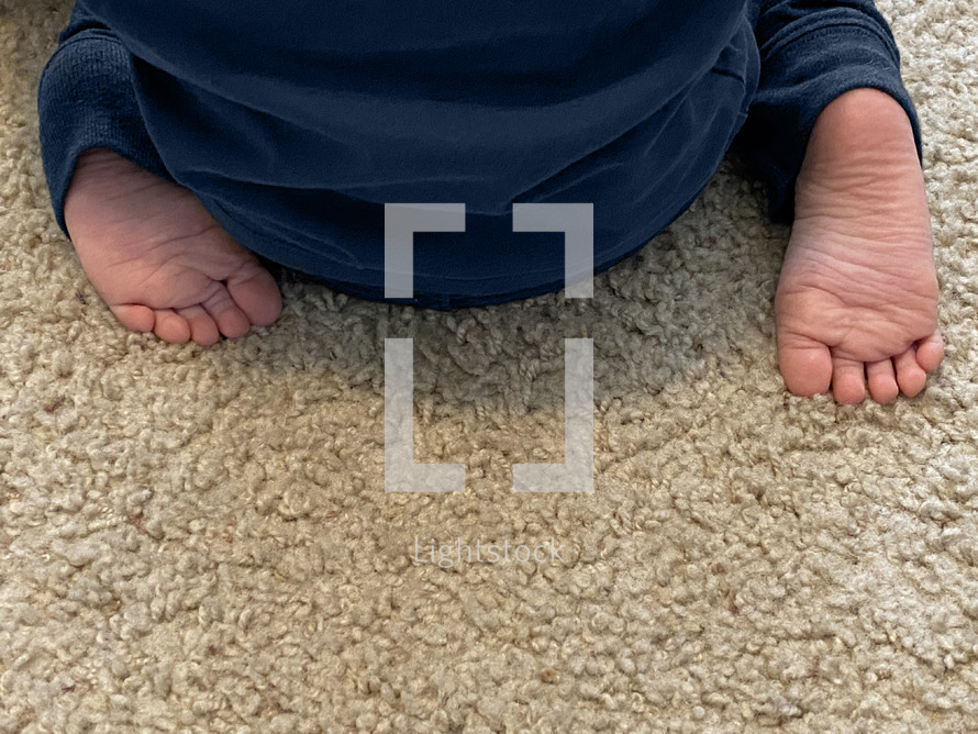 sweet little feet of a small child seated on a carpeted floor, viewed from behind